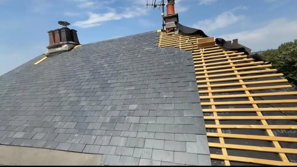 Toiture en ardoise en cours de pose à Bois-Guillaume, avec deux souches de cheminée et des liteaux posés sur l'écran de sous-toiture visibles sur la droite