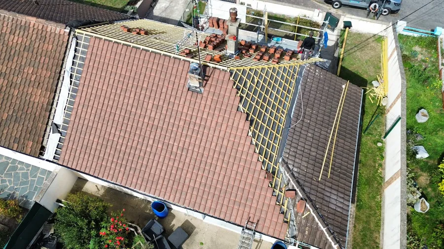 Vue aérienne prise au drone d'une toiture en cours de rénovation : tuiles neuves posées sur une partie du pan, liteaux à nu, échafaudage et couvreur au travail
